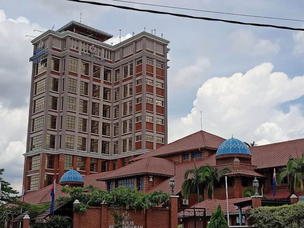 Patil university building exterior with a modern skyscraper and traditional architectural elements, blue domes, greenery, and Malaysia flags, representing academic excellence and cultural heritage in Malaysia.